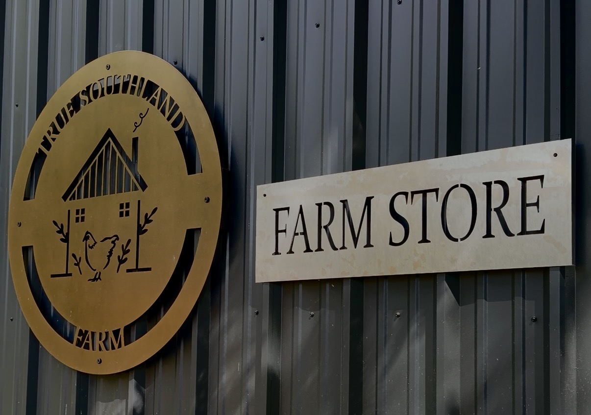 True Southland Farm brass crest and Farm Store sign mounted on dark corrugated metal siding